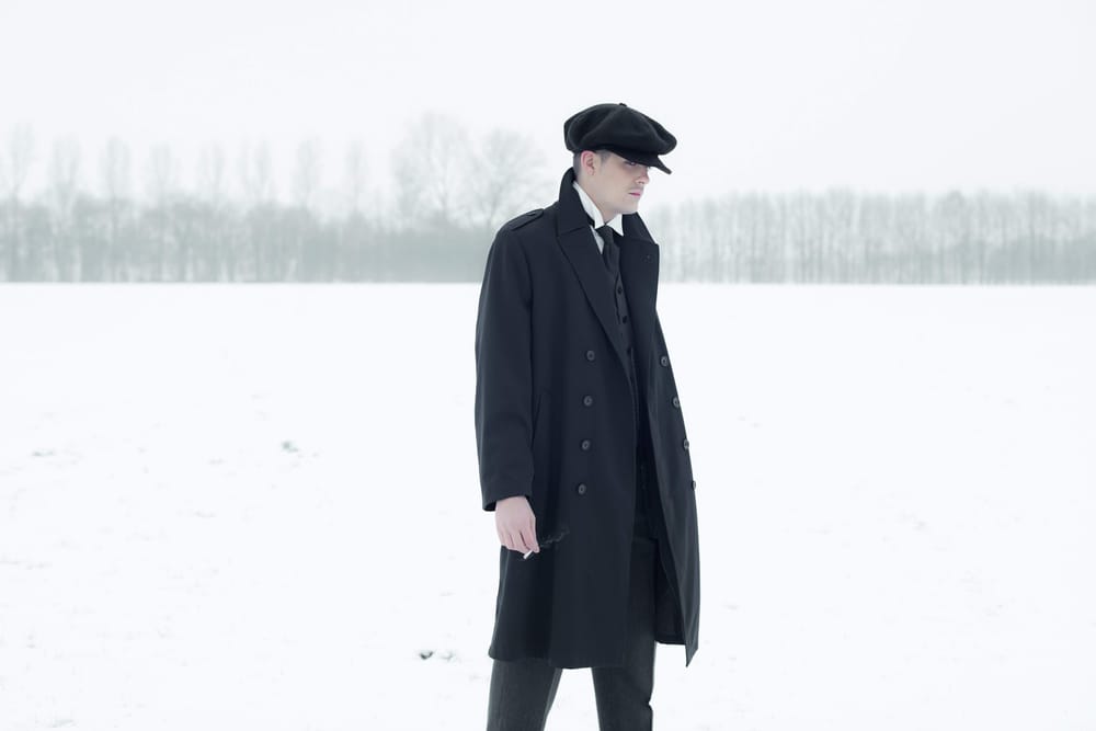 A figure in a long coat and flat cap in the fog